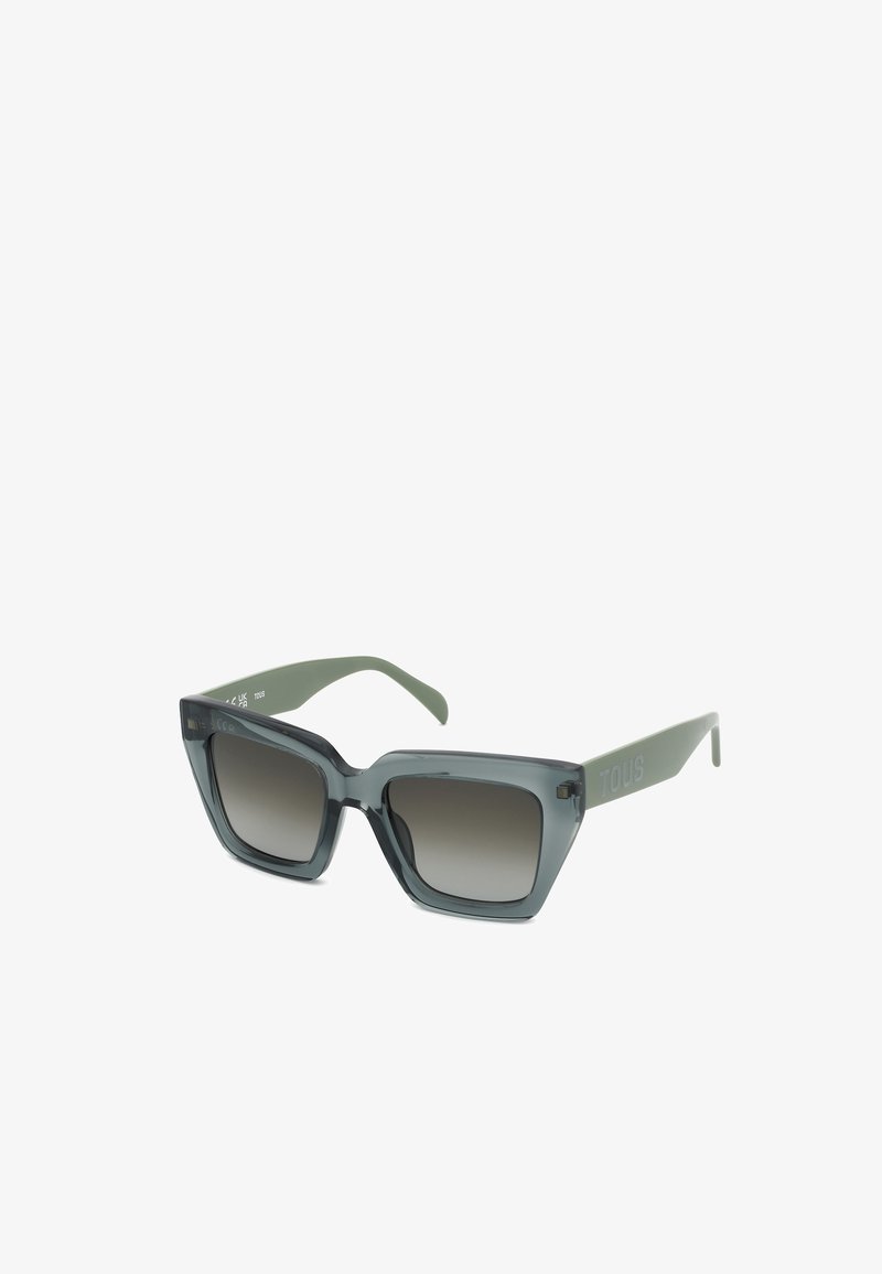 Lunettes de soleil carrées avec des montures épaisses grises et des verres foncés dégradés, avec de larges branches vert olive avec un logo de marque.