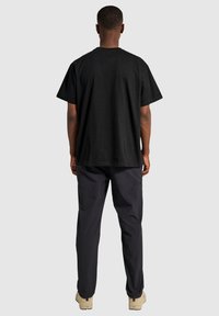 Czarna bawełniana koszulka z krótkim rękawem, luźny krój, okrągły dekolt, noszona z ciemnymi spodniami i jasnymi butami, widok z tyłu.