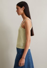 Light green sleeveless top with a ribbed texture, fitted design, and narrow straps. Paired with a blue denim skirt, side view presented.