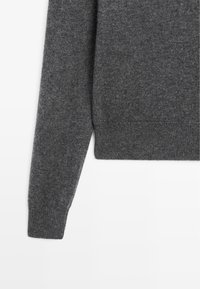 Szary sweter z dzianiny z prążkowanymi mankietami i dołem. Materiał wydaje się miękki i teksturowany, prezentując prosty, elegancki design.