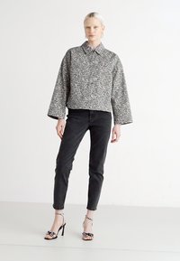 Veste cropped à imprimé léopard gris avec un bouton à l'avant, associée à un jean slim noir et des sandales à talons hauts noires et blanches à motifs.
