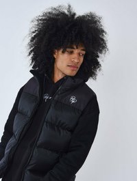 Chaleco acolchado negro con una sudadera con capucha negra sólida debajo. El chaleco presenta un cierre de cremallera y bordado del logo en el pecho.