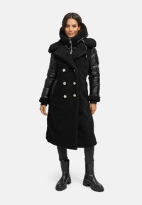 Cappotto nero con esterno morbido, maniche imbottite, design doppiopetto, grandi bottoni e colletto alto, abbinato a stivali neri.