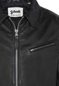 Giacca nera in pelle con collo classico, cerniera frontale e tasca orizzontale con cerniera sul petto. Texture liscia e componenti minimi in metallo.