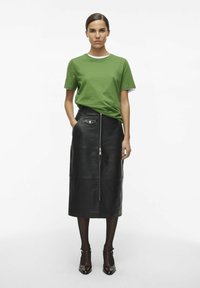 Camisa de algodón verde en capas sobre una falda midi de cuero negra con textura de cocodrilo, que presenta una cremallera central y bolsillos laterales.