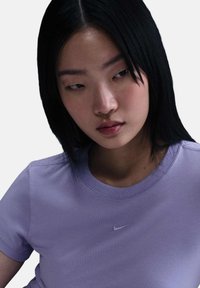 Paarse katoenen T-shirt met ronde hals en korte mouwen, met een klein wit Nike-logo op de borst. Gladde textuur.