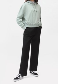 Sudadera corta verde claro con cordones y logo, combinada con pantalones de pierna ancha negros y zapatillas negras con acentos blancos.