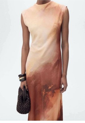 Nádržkové šaty s přechodem barev od béžové po rezavé tóny, nošené s černými a zlatými náramky a texturovanou tmavě hnědou kabelkou.