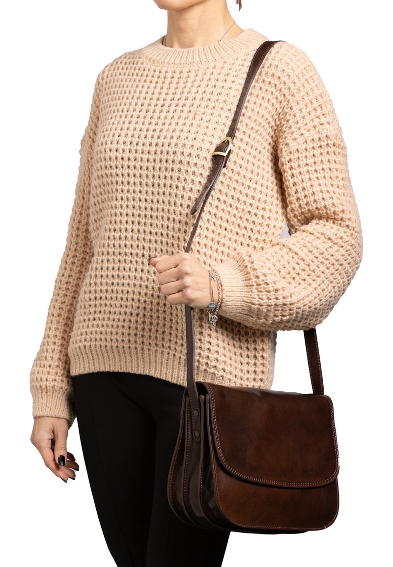 Borsa a tracolla in pelle marrone con patta pieghevole, dettagli di cucitura sottili e una tracolla marrone regolabile, indossata sopra un maglione di colore beige in maglia.