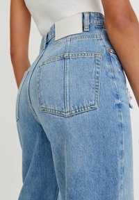 Jeans de mezclilla azul claro con una cintura alta, que cuentan con bolsillos traseros, una etiqueta de cuero en la cintura y un ligero desgaste en el dobladillo.