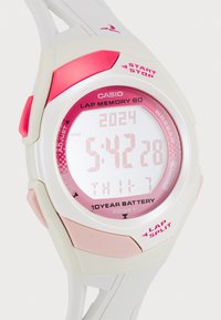 Montre de sport numérique avec un bracelet en caoutchouc blanc et rose, un grand cadran multifonction avec des accents roses, et des boutons pour démarrer, arrêter et réinitialiser.