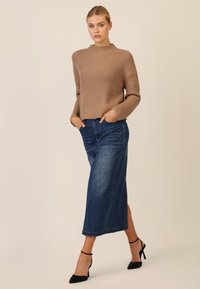 Beige geripptes Sweatshirt mit hohem Kragen, kombiniert mit einem knielangen blauen Jeansrock mit Pünktchenakzenten und schwarzen hohen Schuhen.