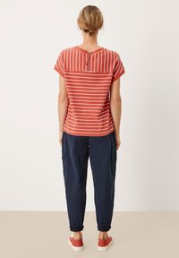 Top de manga corta a rayas rojas y blancas con cremallera en la parte posterior, combinado con pantalones navy y zapatillas rojas. Casual, de corte holgado.