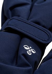 Marinblå, texturerad tyg med en slät yta; har en framträdande vit logotyp och en säker remdesign för funktionalitet.