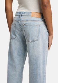 Jeans in denim blu chiaro con una vestibilità rilassata, caratterizzati da un'etichetta in pelle color tan sul retro e due tasche posteriori con cuciture visibili.