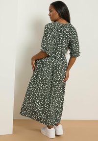 Grön blommig klänning med vita mönster, korta puffärmar, figursydd midja och ankellängd. Kombinerad med vita sneakers.