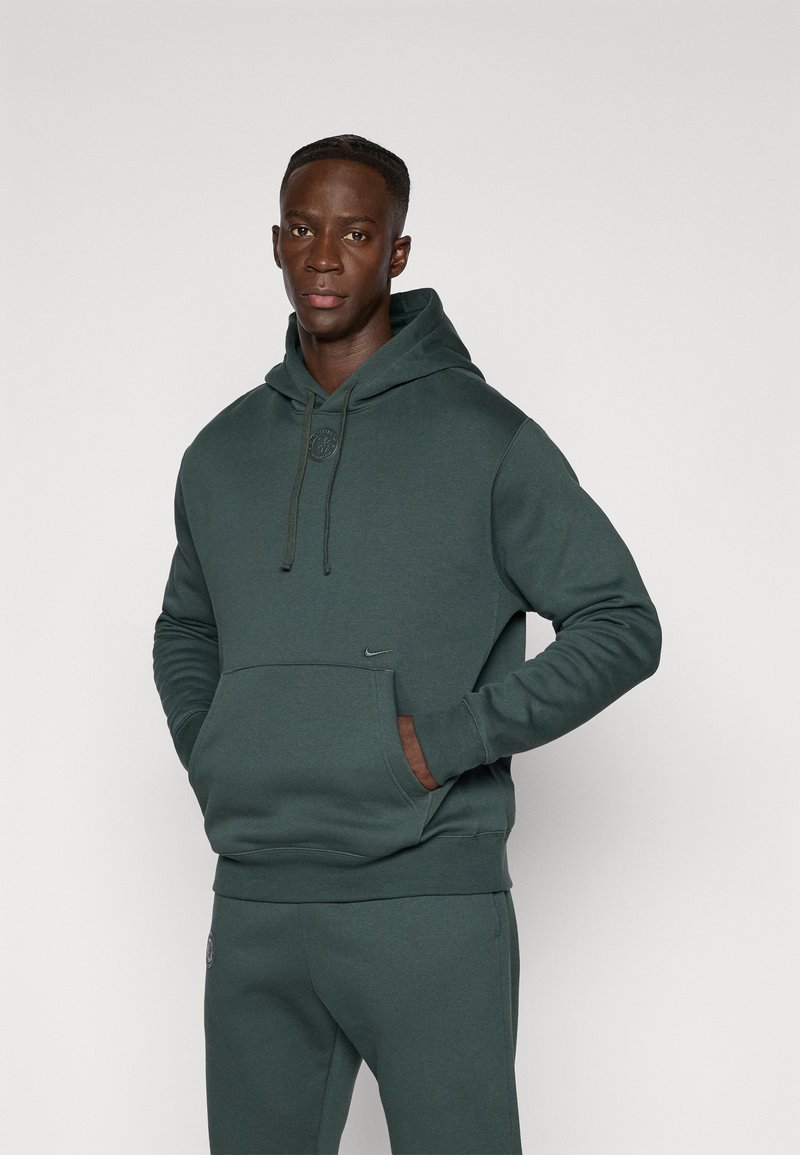Hoodie verde scuro realizzato in morbido tessuto, con tasca frontale, cappuccio regolabile e piccolo logo del marchio sul petto. Taglio aderente.