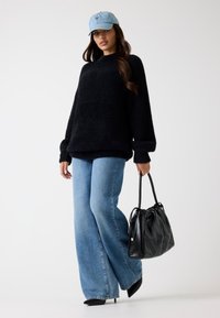 Pull noir texturé ; casquette en denim bleu clair ; jeans larges bleus ; sac à main matelassé noir ; escarpins noirs. Tenue simple et décontractée, avec des détails minimalistes.