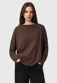 Maglietta marrone a maniche lunghe realizzata in tessuto morbido, con scollo ampio e vestibilità rilassata, abbinata a jeans scuri. Design semplice e contemporaneo.