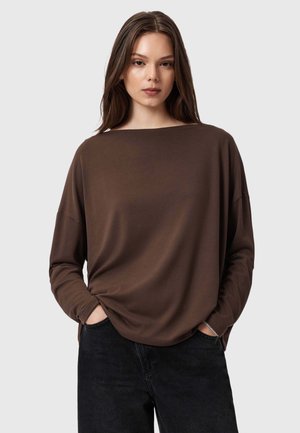 Maglietta marrone a maniche lunghe realizzata in tessuto morbido, con scollo ampio e vestibilità rilassata, abbinata a jeans scuri. Design semplice e contemporaneo.