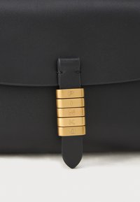 Borsa in pelle nera con texture liscia, caratterizzata da dettagli in metallo dorato con lettere incise e un particolare della tracolla cucita.