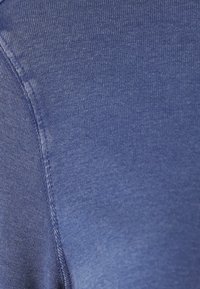 Dunkelblaue Baumwollstoffe mit glatter Textur, die dezente Nahtdetails und ein dehnbares Gefühl aufweisen. Nahaufnahme des Materials.
