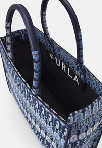 Saco de lona em tons de azul, com um exterior padrão e alças em azul marinho. O interior inclui um bolso com fecho e um detalhe de logotipo.