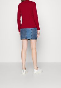 Röd långärmad topp i kombination med en blå denimkjol som har flera tygpaneler och två bakfickor, kompletterad med vita sneakers.