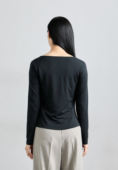 Black long-sleeve top with a square neckline, featuring a soft, smooth texture. Paired with light gray trousers, displayed from the back.