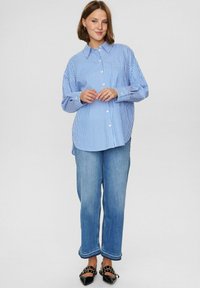Blå och vit randig skjorta med knappar och långa ärmar, i kombination med ljusblå högmidjade jeans och svarta spetsiga skor.