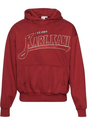 Raudonas džemperis su gobtuvu, pagamintas iš minkštos medvilnės mišinio, su priekinėmis kišenėmis, gipiūro apykakle ir apatine dalimi, su „KARL KANI“ logotipu ir 1989 metų numeriu, atspaustu balta spalva.