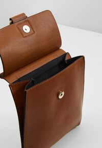 Ruskea nahkalaukku, jossa on sileä pinta, kultainen napin suljenta, avoin osasto ja pehmeä musta vuori. Yksinkertainen suorakulmainen muoto.