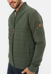 Groene bomberjack met een gequiltde voorkant, ritsluiting, ribgebreide manchetten, leren accent op de mouw en zijzakken voor opberging.