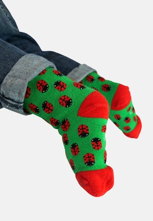 Grüne Socken mit einem Marienkäfer-Muster, roten Akzenten und einfarbigen roten Bündchen. Sie haben eine weiche Textur und ein verspieltes Design.