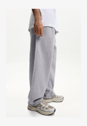 Pantaloni sportivi grigi realizzati in tessuto morbido, con una vestibilità ampia e una cintura elastica. Abbinati a scarpe da ginnastica beige e grigie.