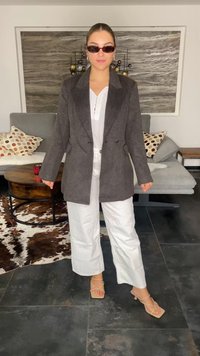 Grauer doppeltknöpfiger Blazer, weiße Bluse und weiße weite Hose. Das Model trägt schwarze Sonnenbrillen und beige Sandalen mit Riemchen. Schlichter, strukturierten Look.