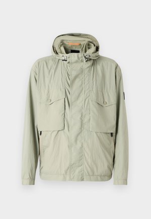 Jaqueta leve de cor verde-claro com capuz, dois bolsos no peito e zíperes laterais. Apresenta uma textura suave e cordões ajustáveis.