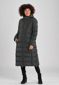 Lange zwarte pufferjas met capuchon, gequiltde textuur, ritssluiting, zijzakken en geribde manchetten. Gecombineerd met zwarte broek en laarzen.