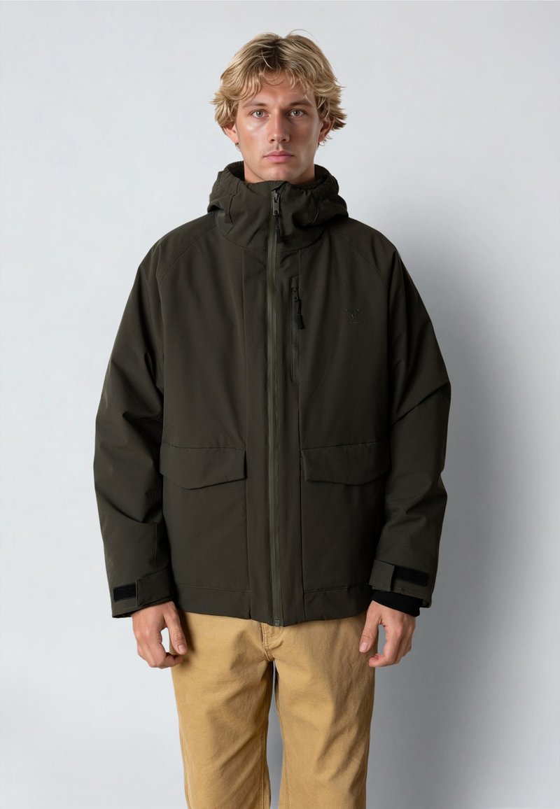 Tumma vihreä vedenpitävä takki, jossa on korkea kaulus, etuvetoketju, kaksi suurta taskua ja säädettävät hihansuut. Rakennekangas ja huppu.