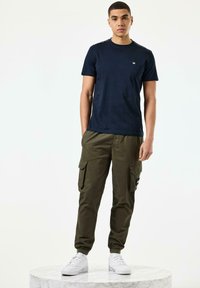 Marine crew-neck t-skjorte, kombinert med olivengrønne cargo-bukser med sidelommer, og hvite sneakers på en marmorpedestal.