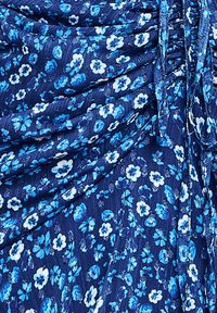 Tissu floral bleu avec de petites fleurs blanches et bleu clair sur un fond bleu foncé, présentant une apparence texturée et légèrement drapée.