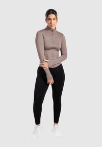 Brun zip-up langærmet top parret med sorte leggings, med en tætsiddende design og blød tekstur. Modellen bærer hvide sneakers.
