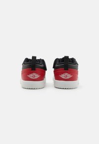 Røde og sorte sneakers med en glat læderfinish, hvide gummisåler og et fremtrædende hvidt logo på hælen. Udstyret med en træksløjfe.