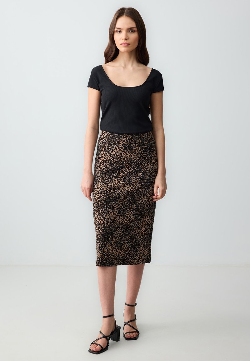 Zwarte geribbelde top en een midi-jurk met luipaardprints met een strakke pasvorm. De rok heeft een soepele textuur en een hoge taille. Zwarte bandjeshakken.
