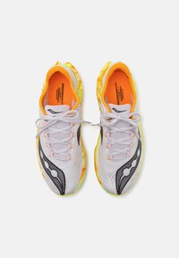Witte mesh hardloopschoenen met oranje accenten, zwarte ontwerp elementen en een gestructureerde gele en groene zool. De veters zijn lichtgrijs.