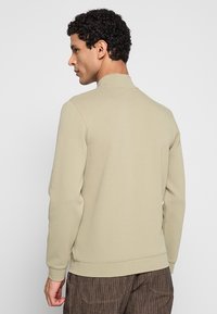Lichtbeige sweatshirt met een hoge kraag en geribbelde manchetten, met een gladde textuur en een losse pasvorm, gecombineerd met gestreepte bruine broek.