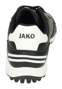 Chaussure de sport noire avec des accents blancs, dotée d'une tige en synthétique, d'un col rembourré et d'un logo JAKO bien visible au niveau du talon. Doublure intérieure texturée.