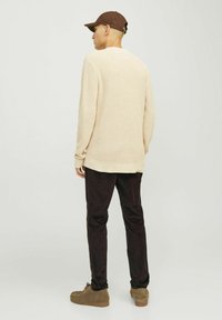 Pull en laine beige avec une texture côtelée, porté sur un pantalon en velours côtelé sombre. Une casquette marron et des chaussures beige complètent la tenue.
