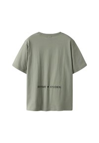 Olive green cotton t-shirt with a relaxed fit, short sleeves, and round neckline. Features black text "REVERY • STUDIOS" on the back.