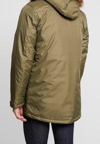 Parka matelassée vert olive avec capuche, présentant une texture lisse, des poignets élastiques et une coupe légèrement allongée pour une meilleure couverture.